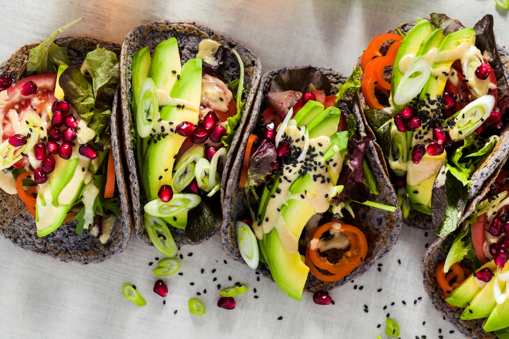 Gluten-free vegan tacos from black bean with tomato and avocado salad with tahini sauce and pomegranate seeds. healthy fast food for the whole family or party